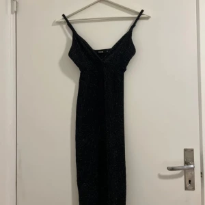 Svart glittrig klänning från Bik Bok - Snygg svart glittrig klänning från Bik Bok i storlek XS. Perfekt för festliga tillfällen med sin figurnära passform och axelbandslösa design. Klänningen har en elegant v-ringning och är tillverkad i ett bekvämt material som ger en lyxig känsla. Ett måste för garderoben om du vill glänsa på nästa fest! ✨