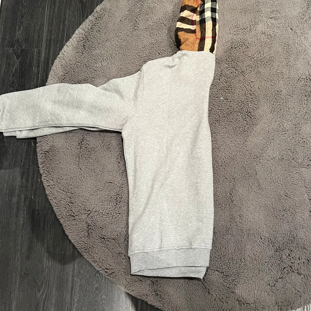 Säljer en snygg grå hoodie från Burberry med den ikoniska rutiga huvan i beige, svart och röd. Helt oanvänd perfekt för höst och vår! Den har dragkedja framtill och är i mycket bra skick. Passar både till vardags och lite finare tillfällen. 🧥✨. Tröjor & Koftor.