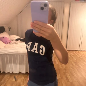 Mörkblå t-shirt från GAP - Säljer en snygg mörkblå t-shirt från GAP i bra skick. Den har en klassisk design med GAP-loggan i vitt på bröstet. Perfekt för en avslappnad stil och passar till det mesta. T-shirten är kortärmad och gjord i ett mjukt material som känns skönt mot huden.