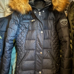 Svart dunjacka från Rockandblue - Säljer en snygg svart dunjacka från Rockandblue med pälskrage. Jackan har en quiltad design och dragkedja framtill. Perfekt för kalla vinterdagar! 🖤