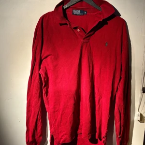 Röd pikétröja från Ralph Lauren - Säljer en klassisk röd pikétröja från Ralph Lauren i storlek M men passar L bra. Tröjan har långa ärmar och den ikoniska broderade loggan på bröstet. Perfekt för både vardag och festliga tillfällen. Skön och stilren design som aldrig går ur tiden. Passa på att fynda! Det har inga defekter eller liknande. Köpt för 1500kr på NK. Tveka inte att höra av dig om du har frågor eller vill ha fler bilder!