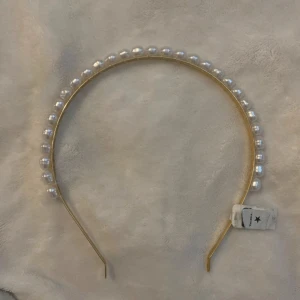 Guldigt diadem med pärlor - Snyggt diadem i guld med vita pärlor som ger en elegant touch. Perfekt för att piffa upp vilken outfit som helst, oavsett om det är till fest eller vardag. Diademet är i nytt skick och har en stilren design som passar alla säsonger.