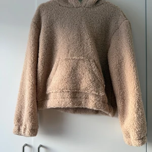 Beige fleece hoodie - Mysig beige hoodie i fleece-material som är perfekt för kyliga dagar. Den har en stor ficka framtill och en bekväm huva. Tröjan är i bra skick och passar perfekt för höst och vinter.