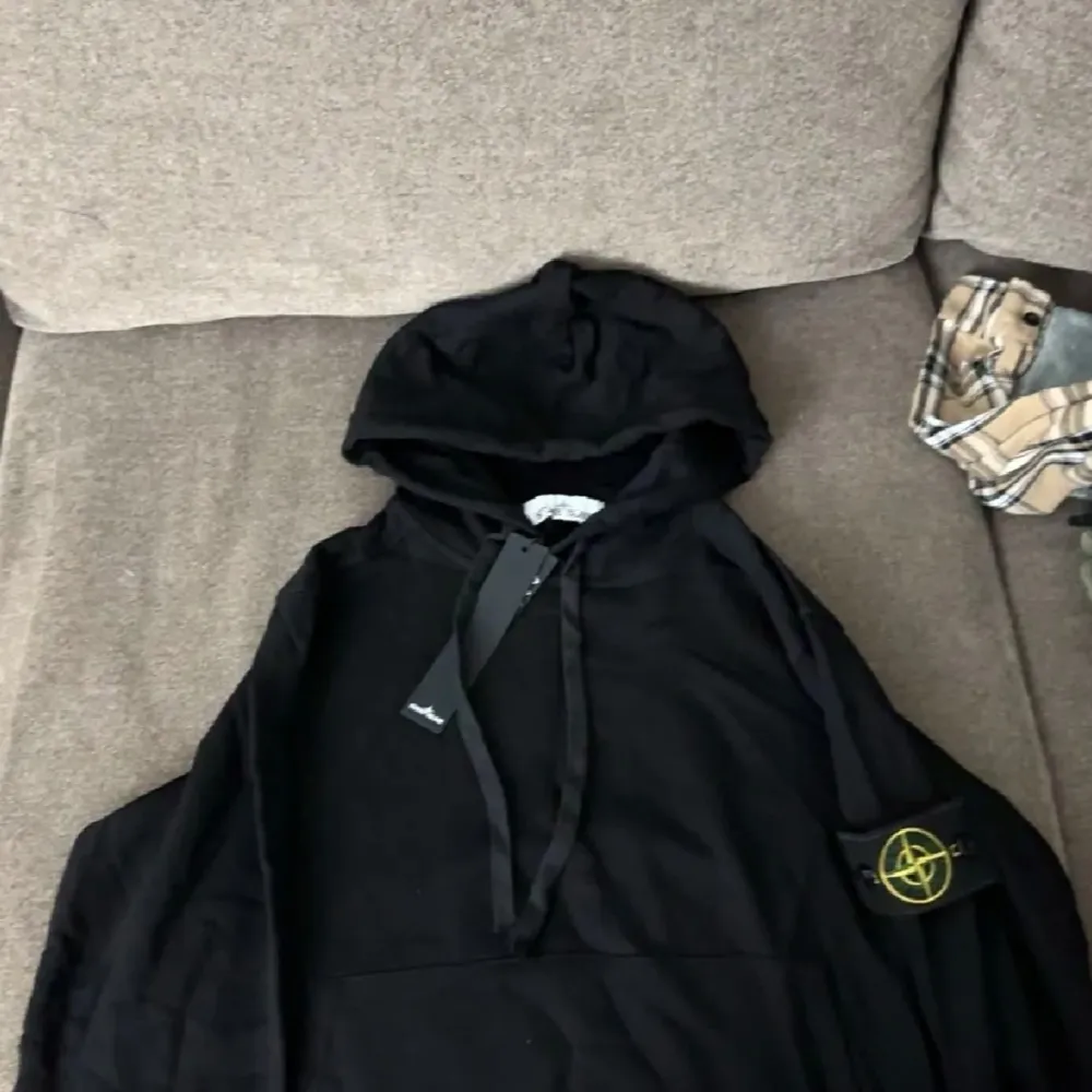 Säljer en snygg svart hoodie från Stone Island. Den har en klassisk design med huva och en ikonisk logga på ärmen. Perfekt för en casual look eller att bara mysa i. Helt ny med taggar kvar!. Tröjor & Koftor.