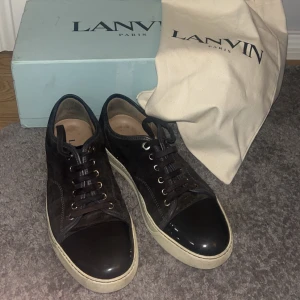 Svarta sneakers från Lanvin - Säljer ett par snygga svarta sneakers från Lanvin. De har en stilren design med svarta snören och en glansig tå. Skorna är i bra skick med lite slitage på sulorna. Perfekta för både vardag och fest! Kommer med originalkartong och dustbag. Skorna har inte blivit ordentligt tvättade, så det går att få bort värsta om man vill. Storlek 40 men passar 41