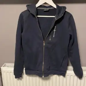 Säljer en snygg mörkblå hoodie från Sail Racing i bra skick. Den har en dragkedja framtill och en bekväm huva. Perfekt för höst och vår, eller när du bara vill ha något mysigt att dra på dig. Passar både till vardags och lite mer avslappnade tillfällen. Fundera inte att fråga om de är nått😼