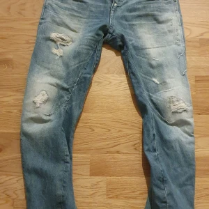 Blå jeans från G-Star - Säljer ett par snygga blå jeans från G-Star i storlek 25/32. De har en cool slitning på framsidan och är i en klassisk denimstil. Perfekta för en avslappnad look! 🕶️
