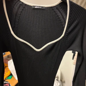 Svart ribbad klänning från Gina Tricot - Säljer en snygg svart ribbad klänning från Gina Tricot. Den har en v-ringad design med kontrasterande vita kanter.