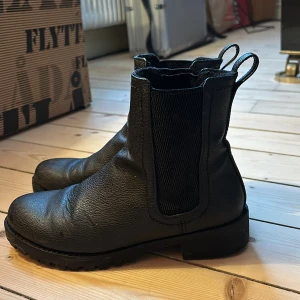 Svarta boots i skinn - Säljer ett par svarta boots i skinn, storlek 37. De har en robust design med elastiska paneler på sidorna för enkel på- och avtagning. Perfekta för höst och vinter med en stilren look som passar till det mesta. Använda men i bra skick.
