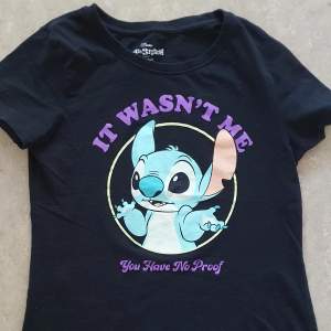 Säljer en svart t-shirt med ett roligt tryck av Stitch från Disney. Texten 'It Wasn't Me, You Have No Proof' står i lila ovanför och under bilden. Perfekt för alla Disney-fans! T-shirten är i bomull och har en normal passform med korta ärmar.