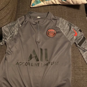 Psg tröja - Säljer en grå fotbollströja från Nike med PSG-logga på bröstet och 'Accor Live Limitless' tryckt på framsidan. Tröjan har ett coolt mönster på ärmarna och 'Visit Rwanda' på ryggen. 