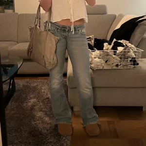 Blå jeans från Lee - Säljer ett par snygga blå utsvängda jeans från Lee i bra skick. De har en klassisk femficksdesign och en bekväm passform. Perfekta för vardagsbruk och kan enkelt matchas med olika toppar och skor. Passar både till avslappnade och mer uppklädda tillfällen. Väldigt lågmidjade och har liten slits längst ner!