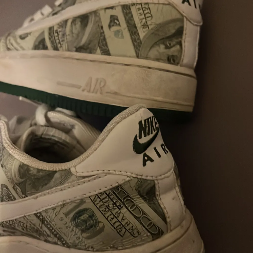 Säljer ett par unika Nike Air Force med ett coolt dollartryck över hela skon. De har en vit bas med gröna detaljer och klassisk snörning. Perfekta för att sticka ut i mängden! Skorna är i bra skick och redo för nya äventyr.. Skor.