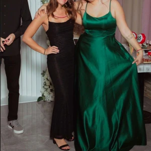 Svart långklänning med spetsdetaljer - Elegant svart långklänning med smala axelband och vacker spets. Klänningen har en tight passform med lite flow nertill. Perfekt till bal eller festtillfällen. 