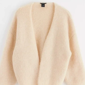 Beige kofta från Lindex  - Mysig beige kofta från Lindex i storlek M. Perfekt för höst och vinter med sin fluffiga och varma design. Koftan har en öppen front och långa ärmar, vilket gör den superbekväm och lätt att matcha med olika outfits.