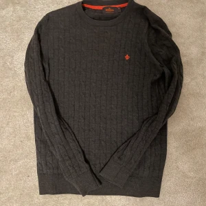 Mörkgrå stickad tröja från Morris - Säljer en snygg mörkgrå stickad tröja från Morris i storlek XS. Tröjan har ett diskret kabelstickat mönster och en broderad orange detalj på bröstet. Perfekt för höst och vinter med långa ärmar och ribbade muddar. Inga större defekter. Nypris ligger på runt 1700kr. I