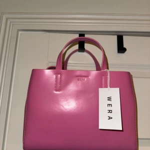 Rosa läder handväska från Wera - Säljer en superfin rosa handväska från Wera i skinn. Väskan är oanvänd och har en stilren design med två handtag och en avtagbar axelrem. Perfekt för både vardag och fest! 💖Höjd: 20cm, bredd ca. 26cm. Nypris 1199kr. 