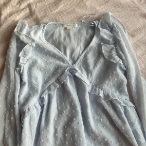 Ljusblå tröja från Gina Tricot - Säljer en superfin ljusblå tröja från Gina Tricot i storlek 146/152. Tröjan har ett sött prickigt mönster och volangdetaljer. Den är långärmad och perfekt för vår och sommar. Passar både till vardag och festliga tillfällen!