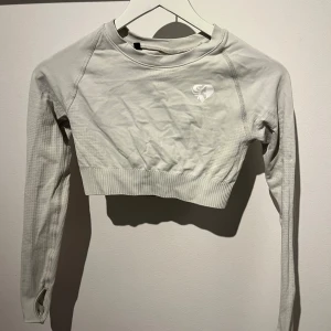 Creme vit croppad tröja från Women's Best - Säljer en snygg creme vit croppad tröja från Women's Best. Perfekt för träning eller en casual look. Tröjan har långa ärmar och en ribbad nederkant som ger en skön passform. Den är i bra skick och redo för nya äventyr! 💪