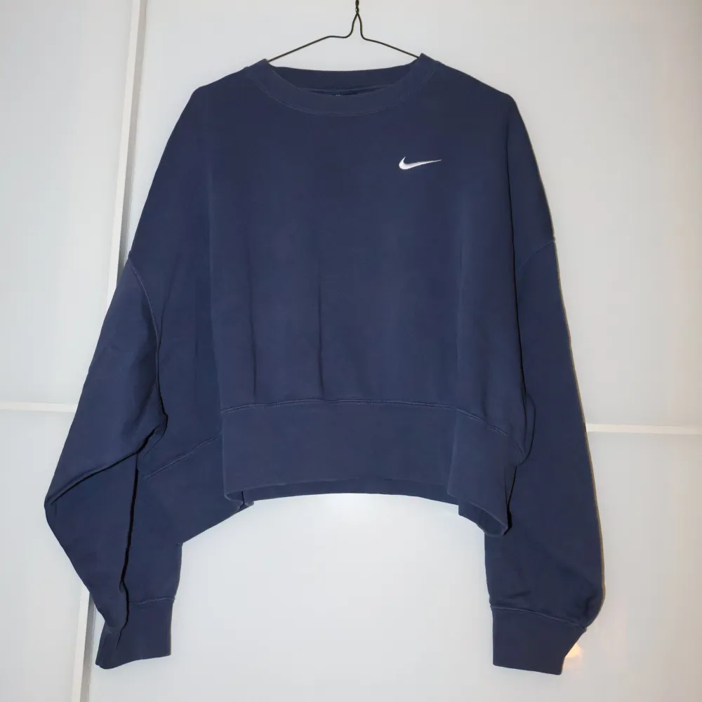 Säljer en snygg blå croppad sweatshirt från Nike. Den har en klassisk rund halsringning och det ikoniska Nike-loggan broderad i vitt på bröstet. Perfekt för en avslappnad stil eller träning. Superbekväm och i bra skick!. Tröjor & Koftor.