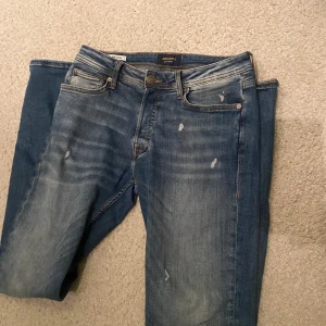 Blå jeans med slitningar - Säljer ett par snygga blå jeans från Jack & Jones i bra skick. De har en slim passform och snygga slitningar