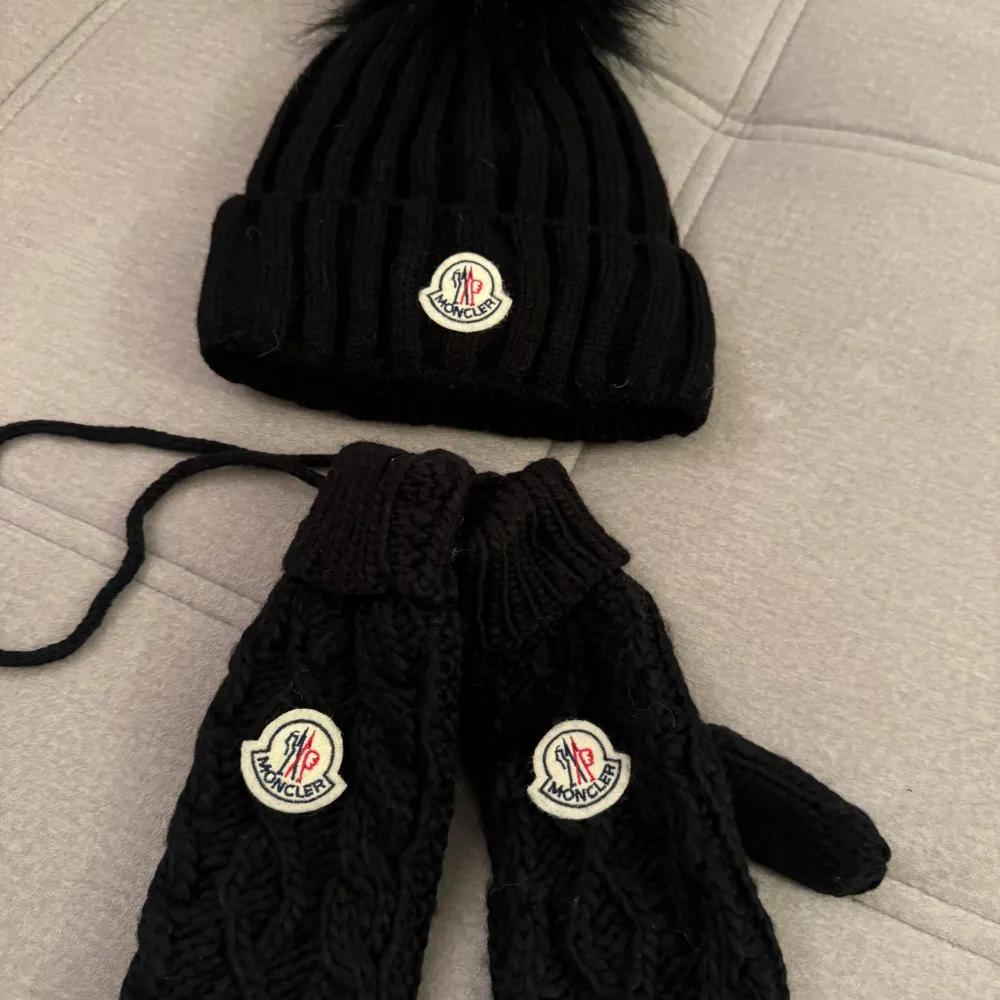 Snygg svart ribbad mössa från Moncler med en fluffig pälsboll på toppen. Perfekt för kalla dagar! Den har Monclers ikoniska logga framtill. Passar både till vardags och mer uppklädda tillfällen. Håller dig varm och stilren hela vintern.. Accessoarer.