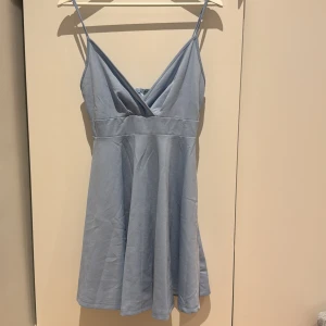 Ljusblå klänning med smala axelband - Säljer en superfin ljusblå klänning med smala axelband och omlott-design framtill. Perfekt för sommardagar eller en avslappnad fest. Klänningen har en luftig passform och är tillverkad i ett mjukt material som känns skönt mot huden. Storleken är S🩷