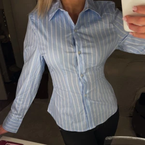 Blå och vit randig skjorta - Säljer denna croppade skjortan då den aldrig kommit till användning, köptes för ett år sen så finns inte kvar längre. Den är väldigt stretchig och skön🤍🩵
