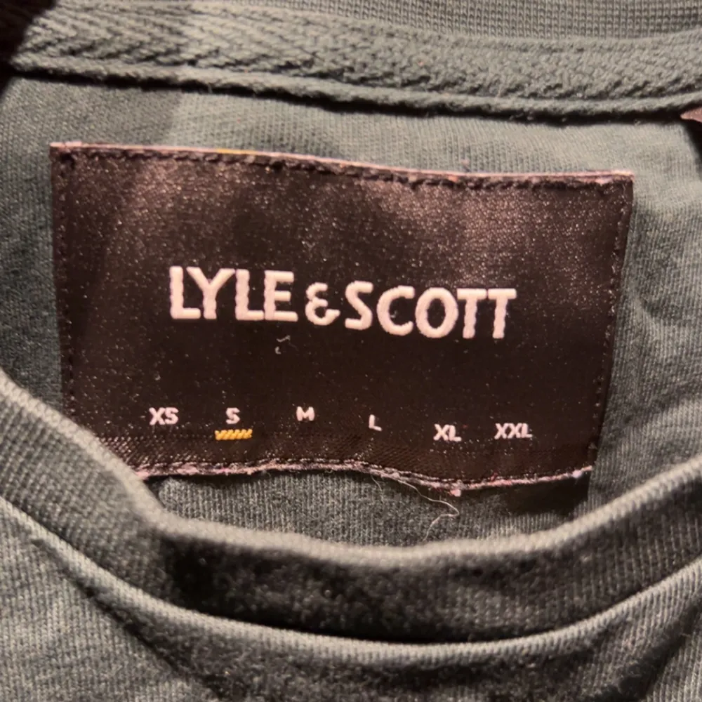 Säljer en snygg grön t-shirt från Lyle & Scott i bomull. Den har en liten gul logga på bröstet och är perfekt för vardagsbruk. T-shirten är i bra skick och har korta ärmar. Passar perfekt till både jeans och shorts!. T-shirts.