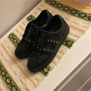 Valentino opens rockstud  - Säljer ett par svarta Valentino sneakers i bra skick. De har coola nitar som ger en edgy look och är perfekta för både vardag och fest. Skorna är i skinn och har en klassisk design med snörning. Passar perfekt för dig som vill ha något unikt i garderoben! Använda ett par gånger men ser helt nya ut. Nypris 6-8000kr Skriv för mer frågor⏳💯🌟