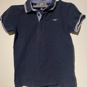 Mörkblå pikétröja från Hampton Republic - Säljer just nu en snygg mörkblå pikétröja från Hampton Republic. Den har korta ärmar och en klassisk krage med vita ränder. Perfekt för både vardag och lite finare tillfällen. Tröjan är i bra skick och redo för en ny ägare! Är i storlek XS, kan passa dom som har S.