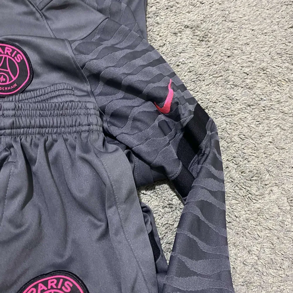 Säljer ett par grå PSG shorts från Nike med snygga rosa detaljer och logga. De har en elastisk midja och dragkedjefickor. Perfekta för fotbollsträningen eller bara för att chilla i. Materialet känns skönt och andas bra. Passar perfekt för sommarens aktiviteter! Priset är ej hugget i sten!. Shorts.