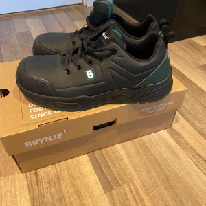 Svarta arbetsskor från Brynje - Säljer ett par svarta arbetsskor från Brynje med snörning och robust design. Skorna har en diskret logga och är perfekta för arbete där säkerhet och komfort är viktigt. Dem är i storlek 40 och har stålhätta som skyddar så man inte skadar sig om man till exempel tappar något på fötterna så kommer man inte skada sig 