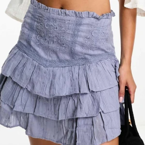 Blå volangkjol - Charmig blå kortkjol med volanger och broderade detaljer. Perfekt för en somrig look med sin lätta och luftiga design.