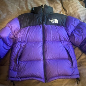 Lila och svart dunjacka från The North Face - Säljer en snygg lila och svart dunjacka från The North Face. Jackan har en dragkedja framtill och är perfekt för kalla dagar. Den är långärmad och har en hög krage för extra värme. XXS men passar XS. Använd många gånger. Nypris: runt 2500 kr. 