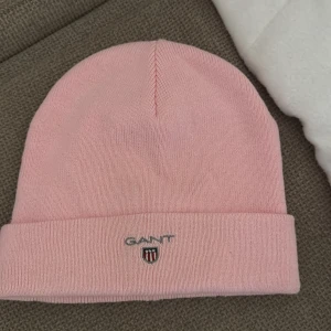 Rosa mössa från GANT - Snygg rosa mössa från GANT med broderad logga framtill. Perfekt för att hålla värmen under kyliga dagar. Enkel och stilren design som passar till det mesta. 