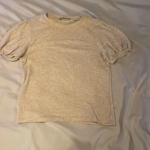 Beige kortärmad topp - Säljer en stilren beige topp med korta puffärmar. Perfekt för en avslappnad look. Materialet är mjukt och bekvämt.