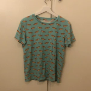 Turkos t-shirt med korvmönster från biltema - Cool turkos t-shirt med ett roligt korvmönster över hela tyget. Perfekt för dig som vill sticka ut med en unik stil. T-shirten har korta ärmar och en normal passform.