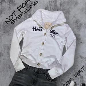 Vit Cardigan Från Hollister - Säljer en vit cardigan från Hollister med knappar och broderad text 'Hollister' på framsidan. Perfekt för en avslappnad stil. Storlek M, passar mer S då den är lite mindre 