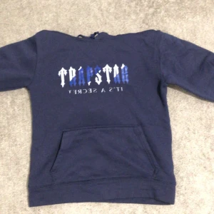 Mörkblå hoodie från Trapstar - Säljer en mörkblå hoodie från Trapstar med texten 'It's a Secret' på framsidan. Tröjan har en klassisk känguruficka och en bekväm huva. Perfekt för en avslappnad stil.