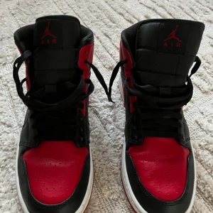 Svarta och röda Nike Air Jordans - Snygga Nike Air Jordans i svart och rött med klassisk design. Skorna har snörning och en hög siluett som ger ett sportigt intryck. Perfekta för dig som vill ha en ikonisk stil.
