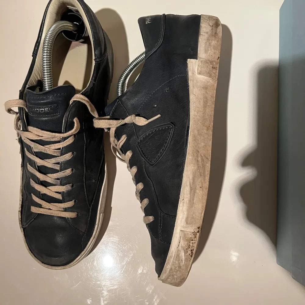 Snygga svarta sneakers från Philippe Model med vita sulor och beige snörning. Perfekta för en stilren look. Skorna har en klassisk design med en diskret logga på sidan. Sparsamt använda. Obs ej og box! Priset är diskuterbart. Kengät.