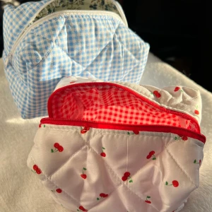 Quiltade necessärer med körsbär och rutor - Två söta quiltade necessärer. Den ena är vit med körsbärsmönster och röd dragkedja, medan den andra har ett blått och vitt rutigt mönster med blommigt foder. Perfekta för att organisera dina småsaker. 199:-/st. Är handgjorda. Skriv innan ni köper 
