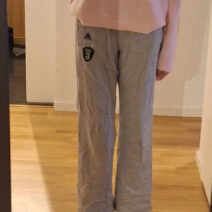 Grå mjukisbyxor från Adidas - Bekväma grå mjukisbyxor från Adidas med en avslappnad passform. Byxorna har en elastisk midja och ett tryckt märke på ena benet. Perfekta för en chill dag hemma eller lätt träning. Är i storlek 152. Är som XS
