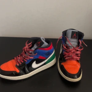 Flerfärgade Nike Air Jordans - Säljer ett par unika Nike Air Jordans i flerfärgad design med inslag av svart, blå, röd, grön och orange. Skorna har en klassisk snörning och den ikoniska Air Jordan-loggan på plösen.