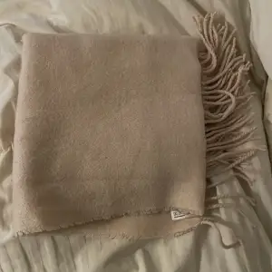 Säljer en stilren beige halsduk från H&M med fransar i ändarna. Perfekt för att hålla dig varm under kyliga dagar. Den är mjuk och bekväm att bära.