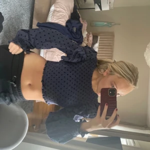 Mörkblå prickig blus - Säljer en mörkblå blus med prickigt mönster och volangdetaljer. Blusen är croppad och har långa ärmar med elastiska ärmslut. Perfekt för en trendig look!