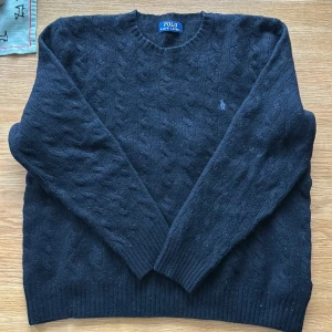Svart kabelstickad tröja från Polo Ralph Lauren - Säljer nu en snygg svart kabelstickad tröja i 10% Kashmir från Polo Ralph Lauren med diskret logga på bröstet.  Den är väldigt bekväm med sitt fina material. Skick skulle jag säga är 8/10. 
