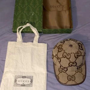 Gucci Jumbo GG Canvas Keps - Säljer en exklusiv Gucci Jumbo GG canvas keps i camel och ebony färg. Kepsen har det ikoniska GG-mönstret och kommer med originalförpackning och dustbag. Perfekt för att ge din outfit en lyxig touch! Digitalt kvitto kommer med. Kan även byta mot en annan Gucci keps! Först till kvarn!!!