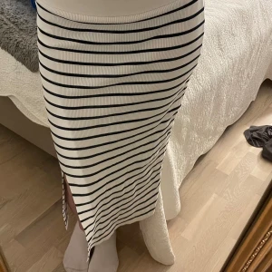 Randig kjol från Holly & White - Säljer en superfin randig kjol från Holly & White i storlek S. Den är vit med svarta ränder och har en liten slits som ger en snygg detalj. Perfekt för både vardag och fest! Kjolen är i mycket bra skick och passar perfekt till vår och sommar.
